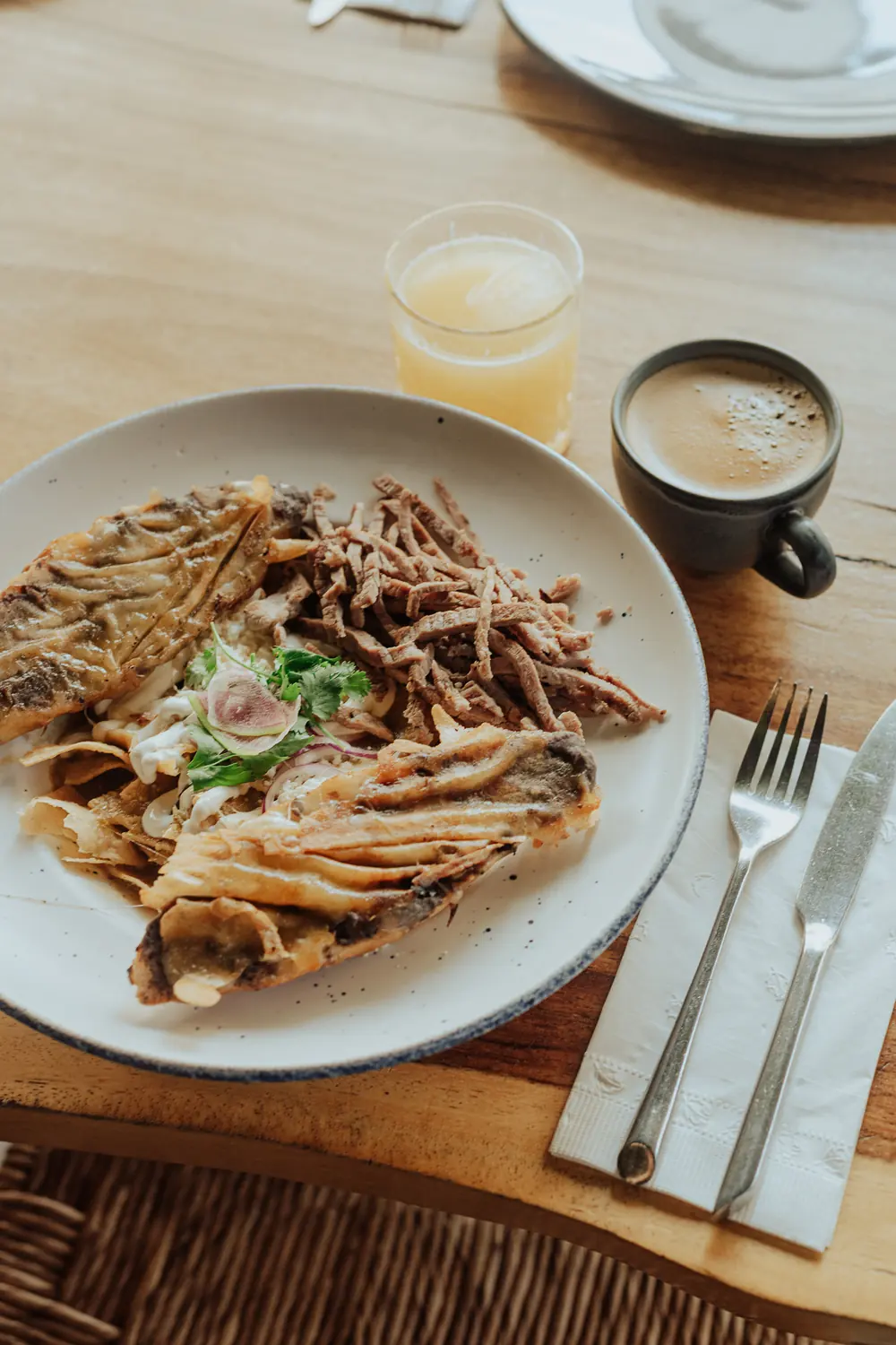 Chilaquiles con cecina, café y jugo, sobre mesa de madera.