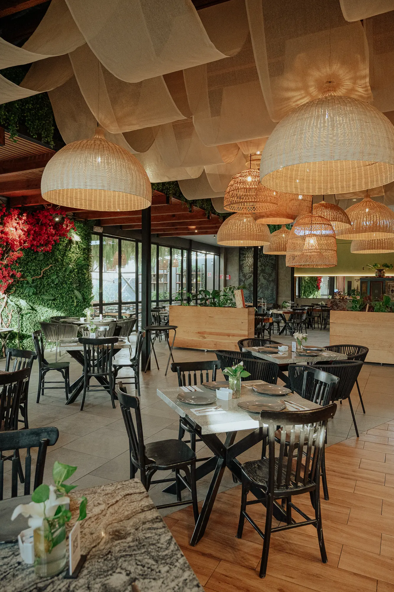 Salón de Los Arbolitos Juriquilla: telas color crema colgadas del techo, lámparas de mimbre y un muro de plantas con bugambilia.