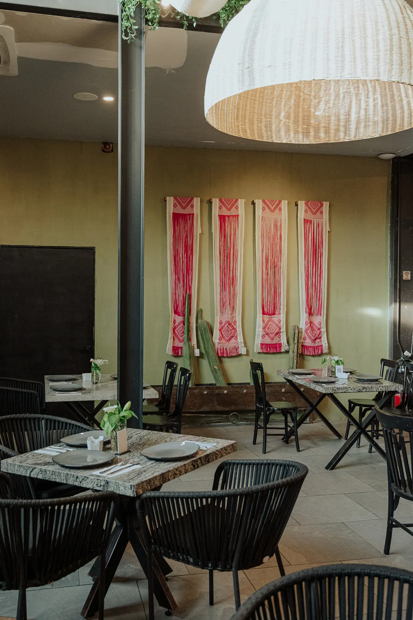 Salón de Los Arbolitos con lámpara de mimbre, cortinas cálidas y muro de plantas.